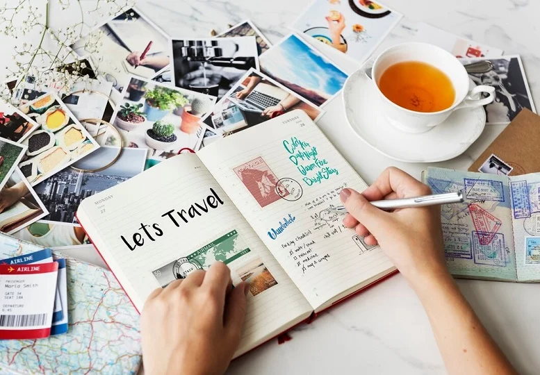 Travel safety planning with a notebook, travel documents, and photographs on a table, alongside a cup of tea.