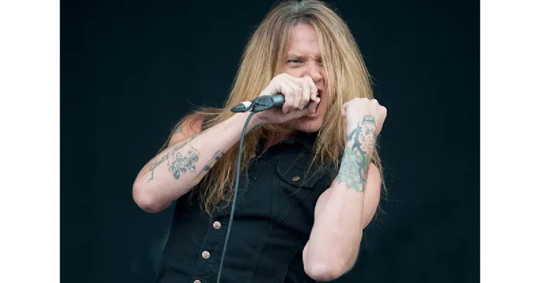 Sebastian Bach performing live on stage with microphone, showcasing his signature long blonde hair and tattoos, former Skid Row frontman known for his powerful vocal range.